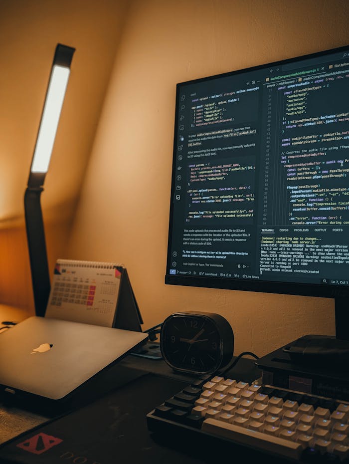 A well-lit home office setup featuring a coding monitor, laptop, and desk accessories.