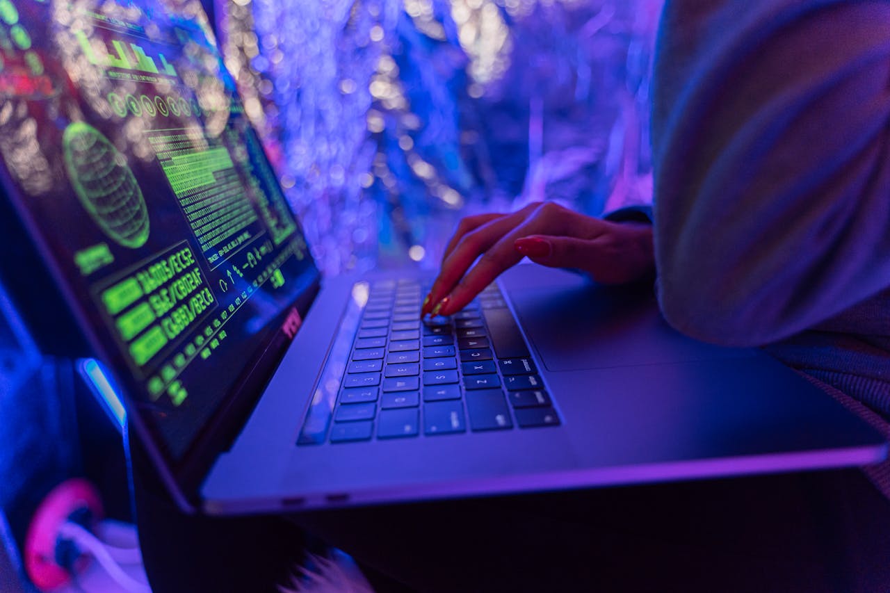 hero-img-01 Close-up of hands typing on a laptop displaying cybersecurity graphics, illuminated by purple light.